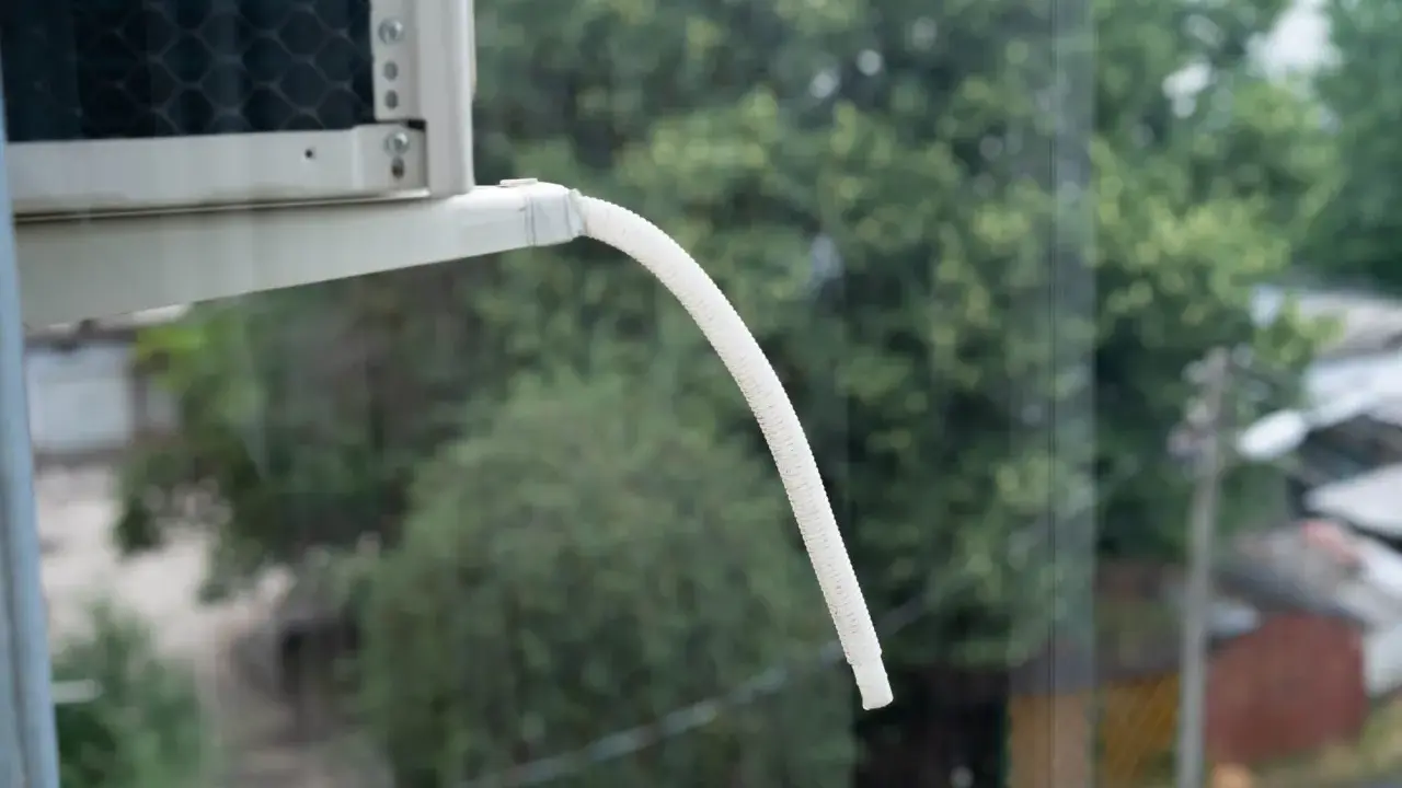 Tubo bianco flessibile per lo scarico condensa condizionatore, sporge da un'unità esterna, con alberi verdi sullo sfondo.