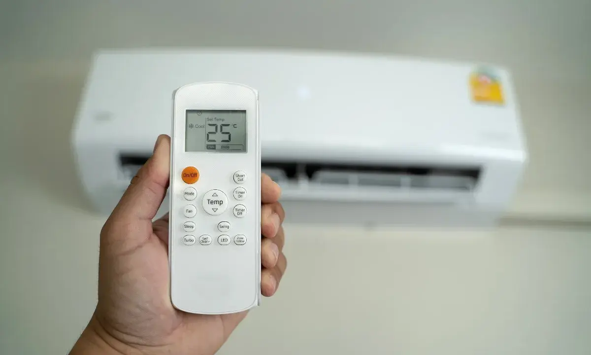 Mano che tiene un telecomando per condizionatore, impostato a 25°C. Il significato di "set temp condizionatore" è la temperatura desiderata.