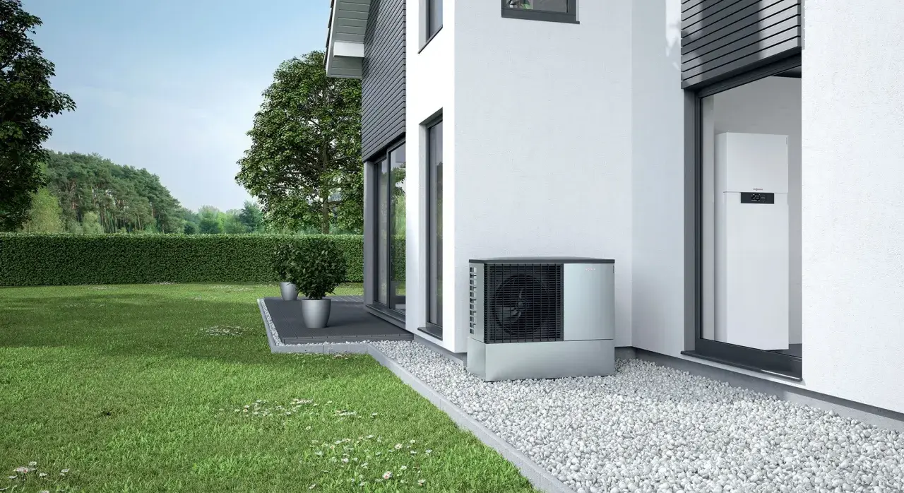 Unità esterna per riscaldamento con condizionatore, posizionata accanto a una casa moderna con giardino curato.
