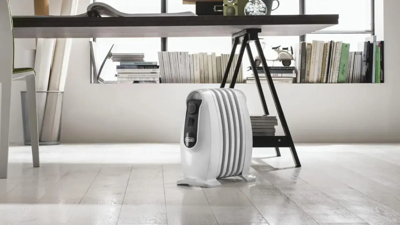 Un radiatore ad olio bianco, sotto una scrivania, mostra come funziona per riscaldare l'ambiente.