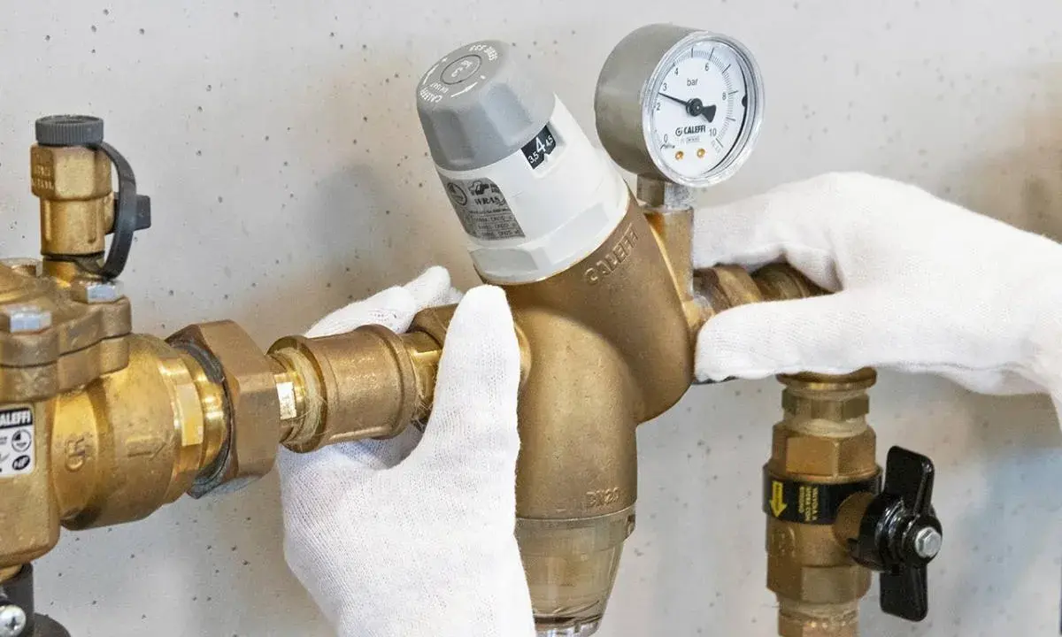 Mani guantate installano un riduttore di pressione acqua, mostrando come funziona con manometro.