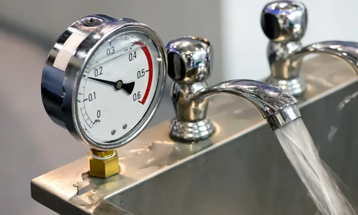 Manometro che misura la pressione acqua rubinetto. Il getto d'acqua scorre nel lavandino.
