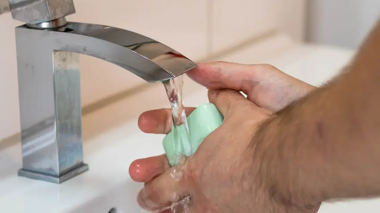 Mani che si lavano sotto un rubinetto cromato, con un getto d'acqua che indica una buona pressione dell'acqua dell'acquedotto.
