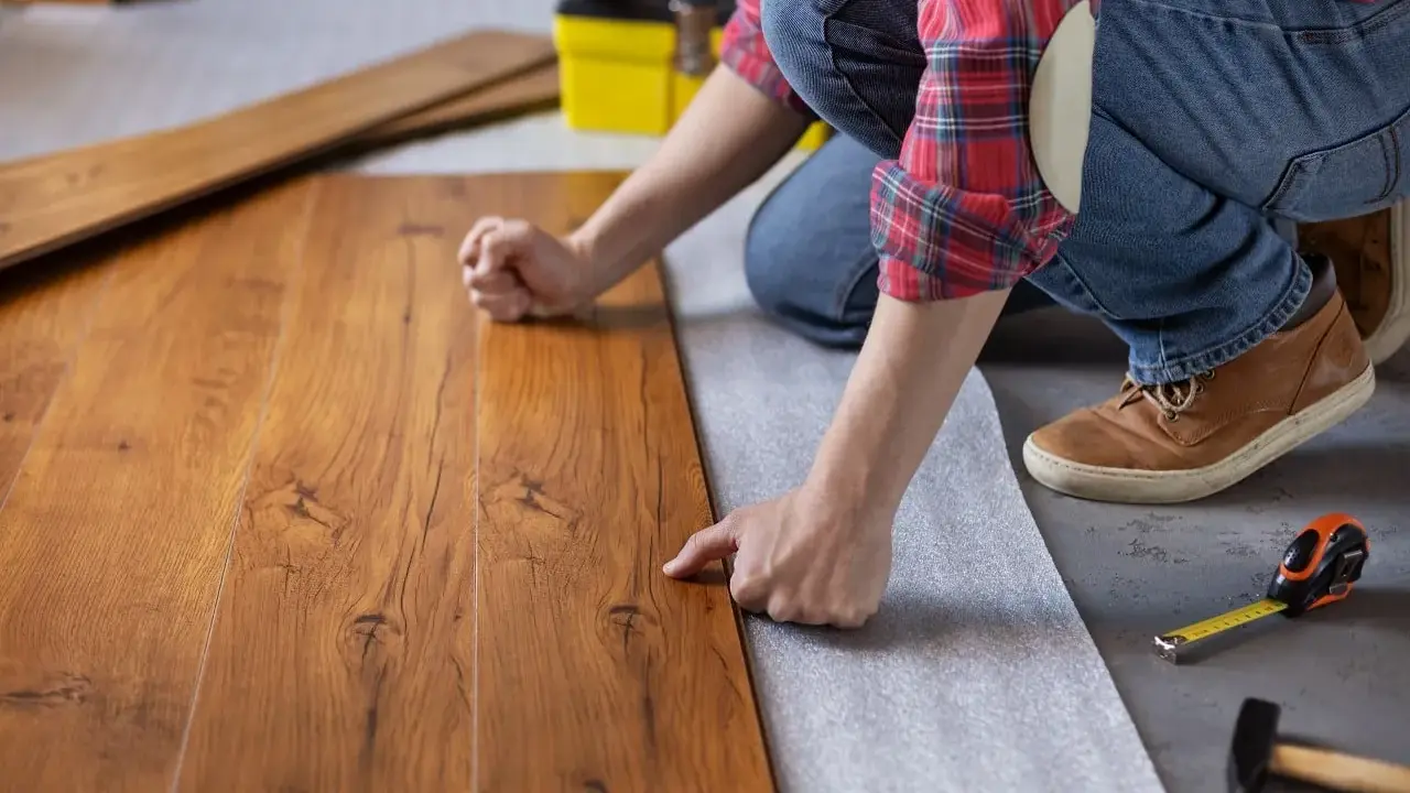 Persona posiziona assi di legno su un tappetino isolante, un passo fondamentale per come insonorizzare il pavimento e ridurre i rumori.