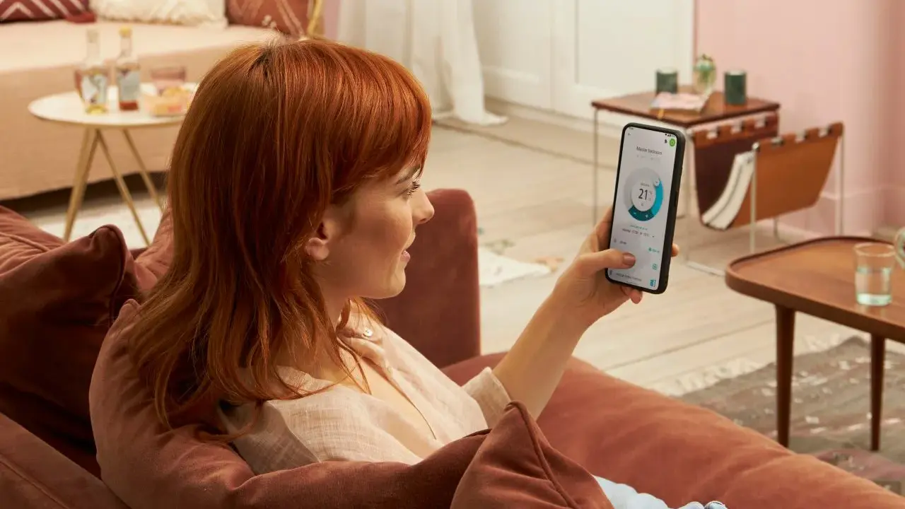 Donna con capelli rossi controlla app Daikin sul telefono, mostrando la differenza tra Daikin e Daikin Siesta per il comfort domestico.