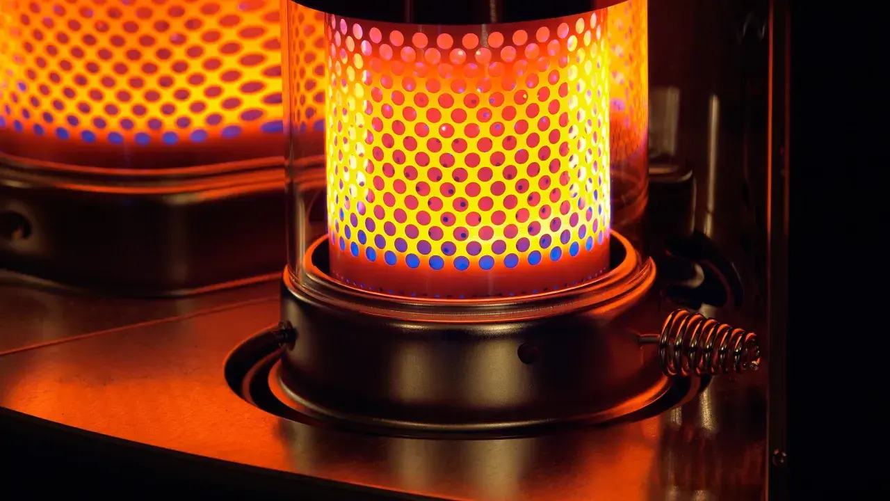 La stufa a kerosene pericolosa emana un calore intenso, con fiamme blu e gialle che danzano attraverso la griglia forata.