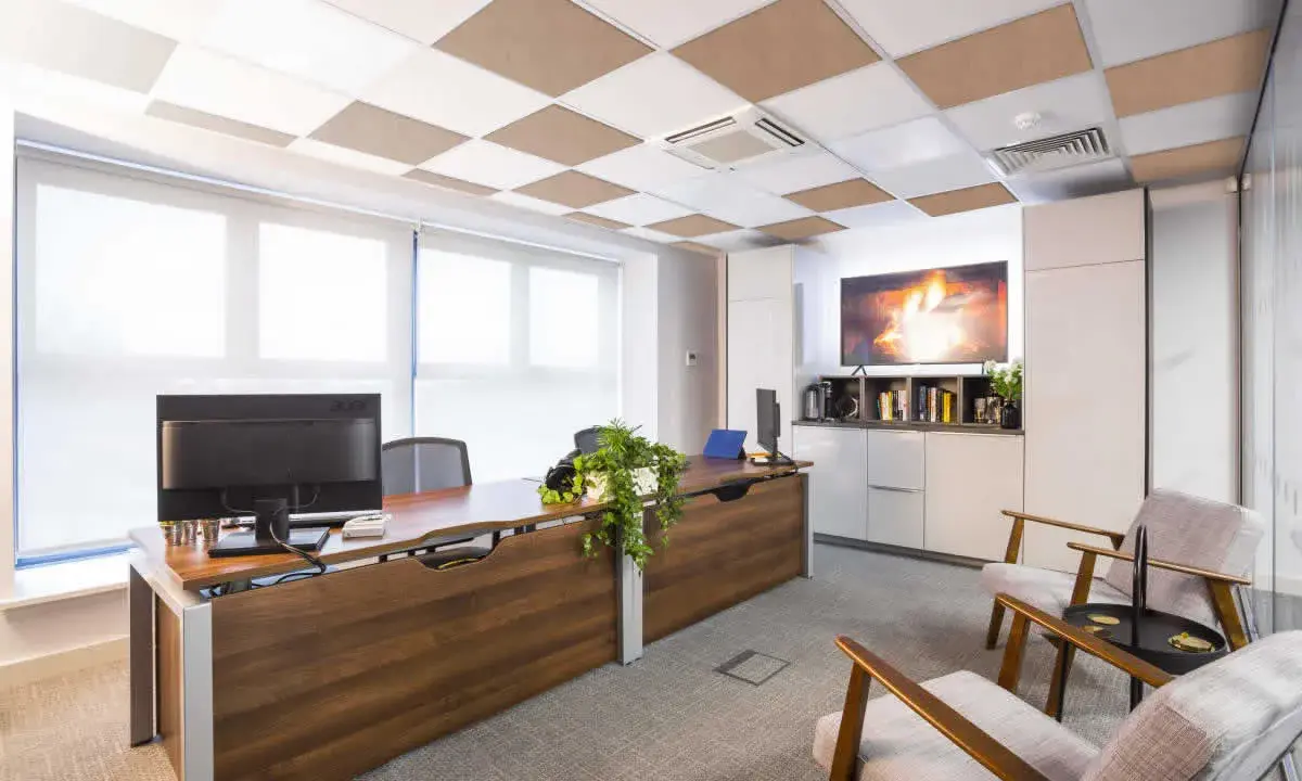 Ufficio moderno con scrivania in legno, computer e due poltrone. Il controsoffitto antirumore a scacchiera bianca e marrone migliora l'acustica.