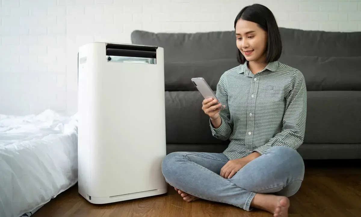 Donna controlla il suo smartphone vicino a un condizionatore portatile, uno dei tanti tipi di condizionatori moderni.