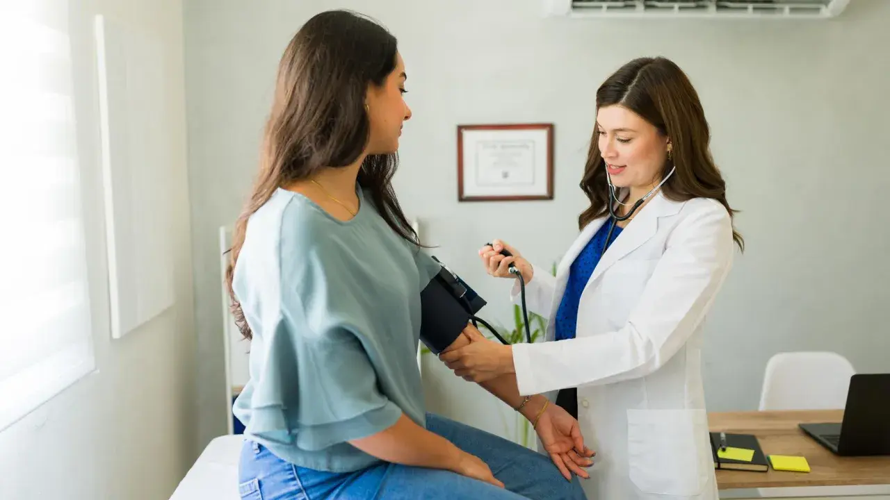 Medico con stetoscopio misura la pressione a una paziente, mostrando come misurare la pressione manualmente.
