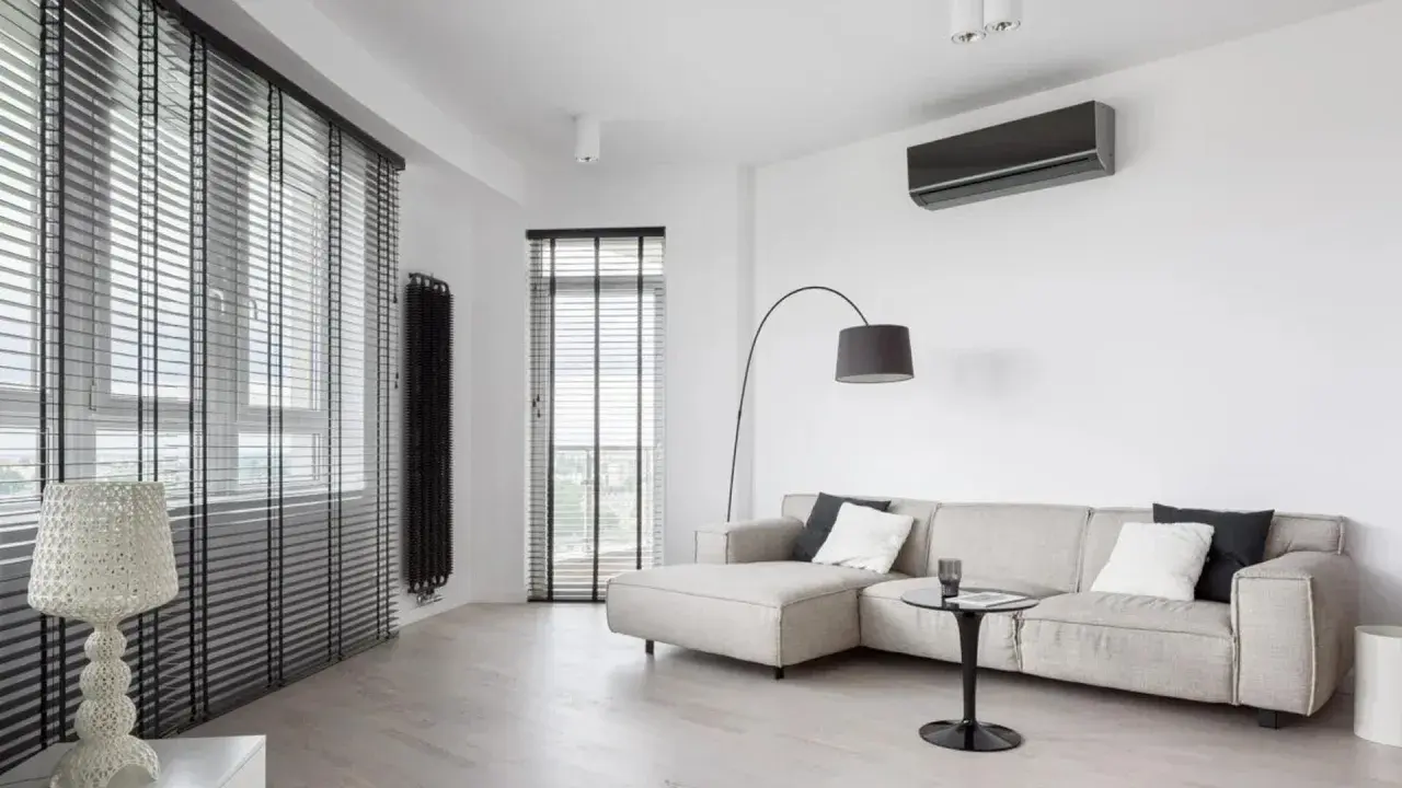 Unità interna di climatizzatore su parete bianca, con divano e lampada. Ideale per capire la differenza tra monosplit e dualsplit.