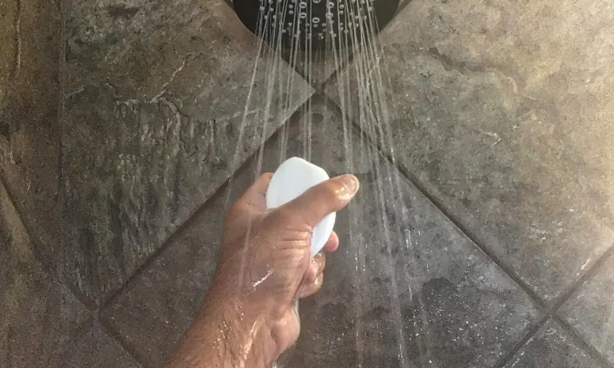 Mano che tiene una saponetta sotto la doccia, con getti d'acqua che suggeriscono il desiderio di aumentare pressione acqua doccia.