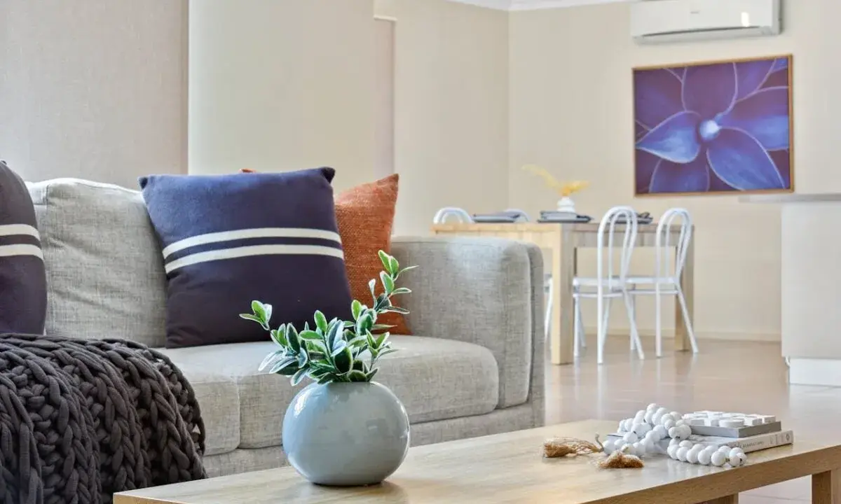 Soggiorno moderno con divano grigio, cuscini decorativi e un condizionatore per rendere smart l'ambiente. Tavolo da pranzo e quadro floreale sullo sfondo.