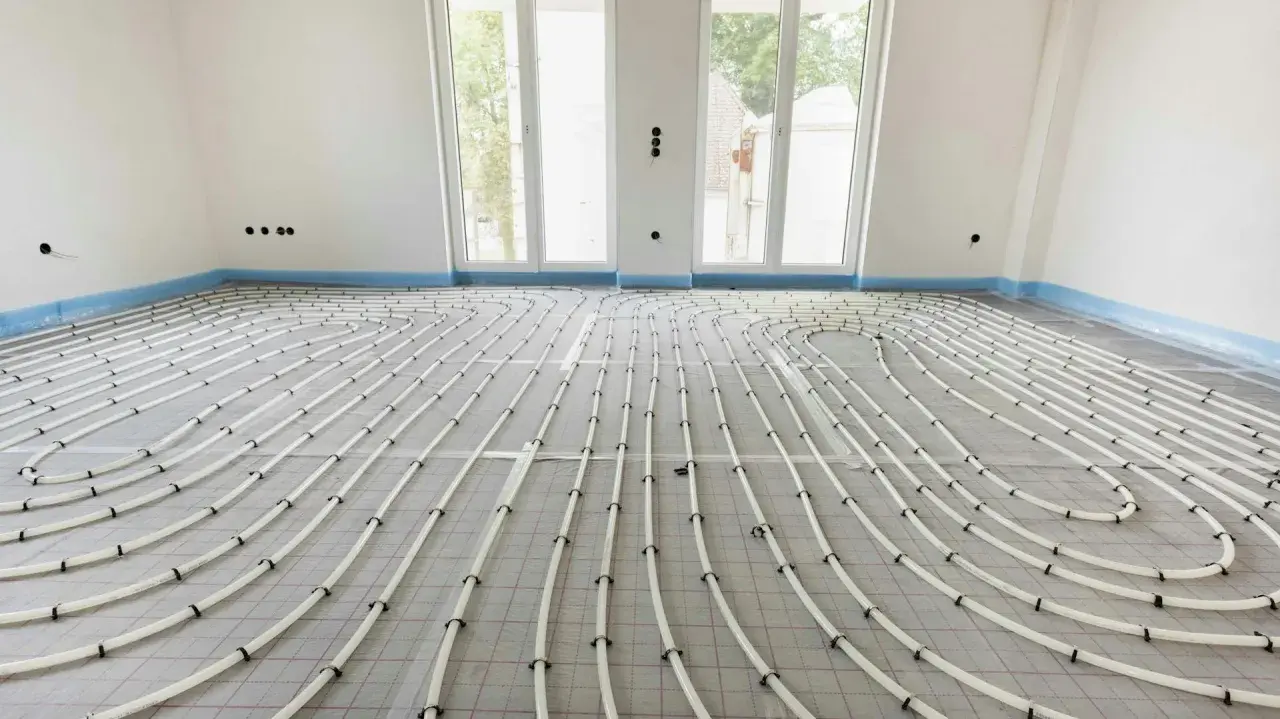 Installazione di riscaldamento a pavimento. Tubi bianchi disposti a serpentina su un foglio isolante, pronti per la posa del massetto. La temperatura dell'acqua sarà regolata per un comfort ottimale.