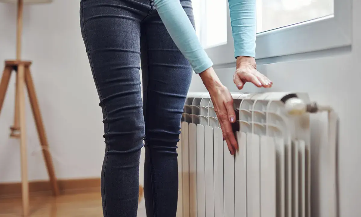 Mani che controllano un termosifone freddo, preoccupazione per il riscaldamento che non funziona.