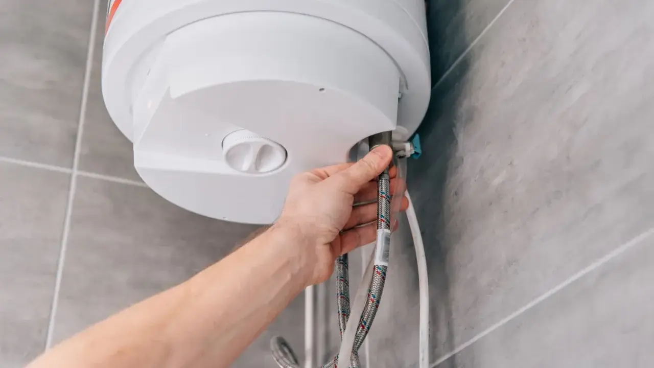 Mano che collega un tubo a uno scaldabagno a gas. La domanda è: quanto dura uno scaldabagno a gas?