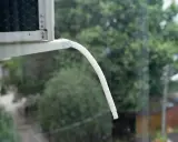 Tubo bianco flessibile per lo scarico condensa condizionatore, sporge da un'unità esterna, con alberi verdi sullo sfondo.