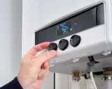 Mano che regola la temperatura su una caldaia a corrente. Il display mostra 76°C.