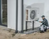 Tecnico che installa un inverter per pompa di calore all'esterno di un edificio.