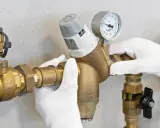 Mani guantate installano un riduttore di pressione acqua, mostrando come funziona con manometro.