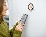 Donna controlla il termostato del riscaldamento tramite smartphone, mostrando come funziona il controllo intelligente della temperatura domestica.