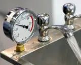 Manometro che misura la pressione acqua rubinetto. Il getto d'acqua scorre nel lavandino.