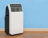 Un condizionatore portatile come funziona: un'unità bianca e nera su ruote, con display digitale, accanto a un muro blu.