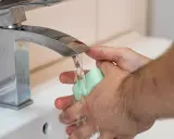 Mani che si lavano sotto un rubinetto cromato, con un getto d'acqua che indica una buona pressione dell'acqua dell'acquedotto.