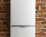 Caldaia Vaillant bianca, con logo, montata su parete in mattoni. Le dimensioni della caldaia sono compatte per adattarsi a spazi ridotti.
