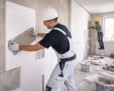 Operai applicano pannelli isolanti su un muro, creando un cappotto interno o esterno per migliorare l'efficienza energetica.