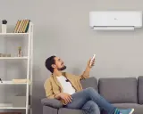 Uomo sorride usando telecomando per accendere un cool condizionatore. Il suo significato è comfort e benessere in casa.
