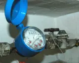 Contatore acqua blu con coperchio aperto, il quadrante è illeggibile per condensa. Tubi e rubinetto arrugginiti.