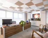 Ufficio moderno con scrivania in legno, computer e due poltrone. Il controsoffitto antirumore a scacchiera bianca e marrone migliora l'acustica.