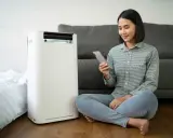 Donna controlla il suo smartphone vicino a un condizionatore portatile, uno dei tanti tipi di condizionatori moderni.