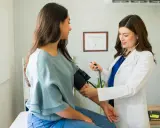 Medico con stetoscopio misura la pressione a una paziente, mostrando come misurare la pressione manualmente.