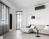 Unità interna di climatizzatore su parete bianca, con divano e lampada. Ideale per capire la differenza tra monosplit e dualsplit.