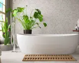 Un bagno umido cosa fare? Una vasca bianca, piante verdi e un tappetino in legno.