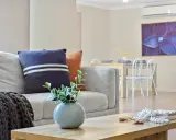 Soggiorno moderno con divano grigio, cuscini decorativi e un condizionatore per rendere smart l'ambiente. Tavolo da pranzo e quadro floreale sullo sfondo.