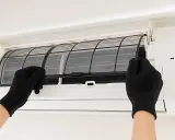 Mani con guanti neri estraggono i filtri da un condizionatore, mostrando come pulire i filtri del condizionatore per un'aria più fresca.