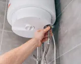 Mano che collega un tubo a uno scaldabagno a gas. La domanda è: quanto dura uno scaldabagno a gas?