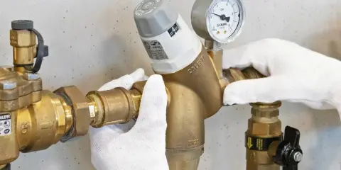 Mani guantate installano un riduttore di pressione acqua, mostrando come funziona con manometro.