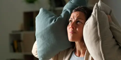 Donna con cuscini sulle orecchie, infastidita da un rumore. Un esempio di 35 decibel, come un sussurro, può disturbare.