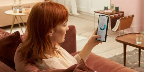 Donna con capelli rossi controlla app Daikin sul telefono, mostrando la differenza tra Daikin e Daikin Siesta per il comfort domestico.
