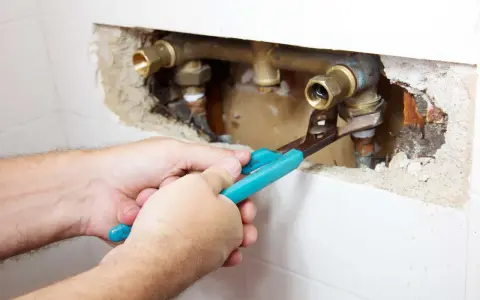 Mani con pinza lavorano su tubature in ottone. Si intravede una valvola di non ritorno prima o dopo la pompa, parte di un impianto idraulico.