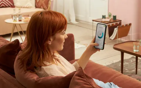 Donna con capelli rossi controlla app Daikin sul telefono, mostrando la differenza tra Daikin e Daikin Siesta per il comfort domestico.
