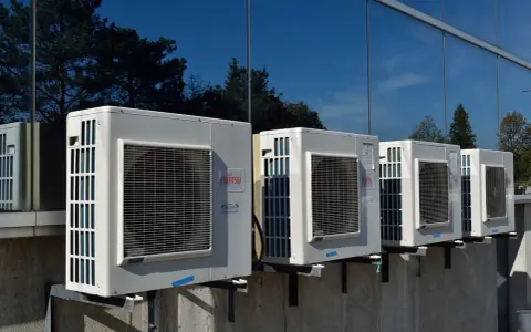 Unità esterne di condizionatori Fujitsu, montate su staffe, riflettono alberi e cielo. Il loro funzionamento è silenzioso, con un basso livello sonoro.