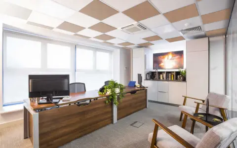 Ufficio moderno con scrivania in legno, computer e due poltrone. Il controsoffitto antirumore a scacchiera bianca e marrone migliora l'acustica.