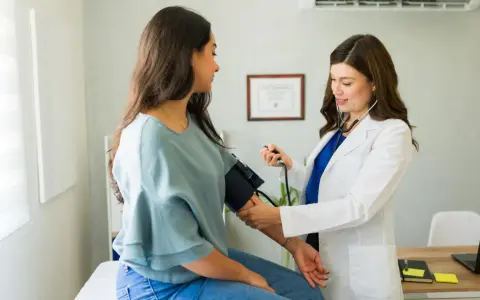 Medico con stetoscopio misura la pressione a una paziente, mostrando come misurare la pressione manualmente.