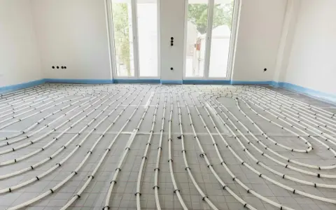 Installazione di riscaldamento a pavimento. Tubi bianchi disposti a serpentina su un foglio isolante, pronti per la posa del massetto. La temperatura dell'acqua sarà regolata per un comfort ottimale.