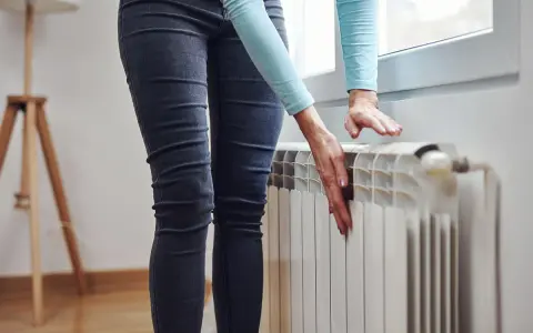 Mani che controllano un termosifone freddo, preoccupazione per il riscaldamento che non funziona.
