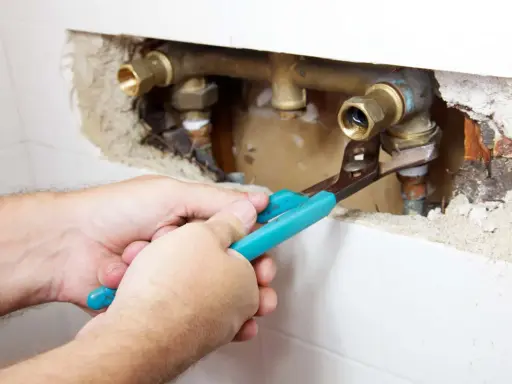 Mani con pinza lavorano su tubature in ottone. Si intravede una valvola di non ritorno prima o dopo la pompa, parte di un impianto idraulico.